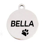 A round silver metal pet ID tag with a hanging loop at the top, featuring the name 'BELLA' in bold black letters and a black paw print below it, shown on a plain white background.